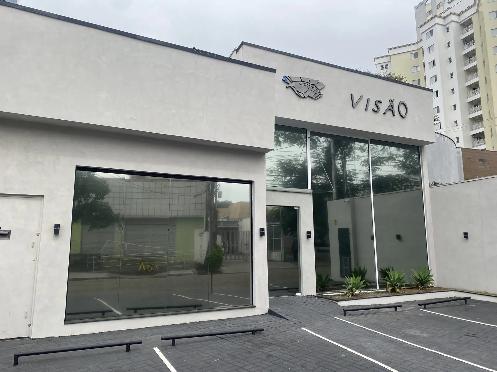 Fachada branca da clínica Visão com o letreiro em relevo e vagas de estacionamento na frente
