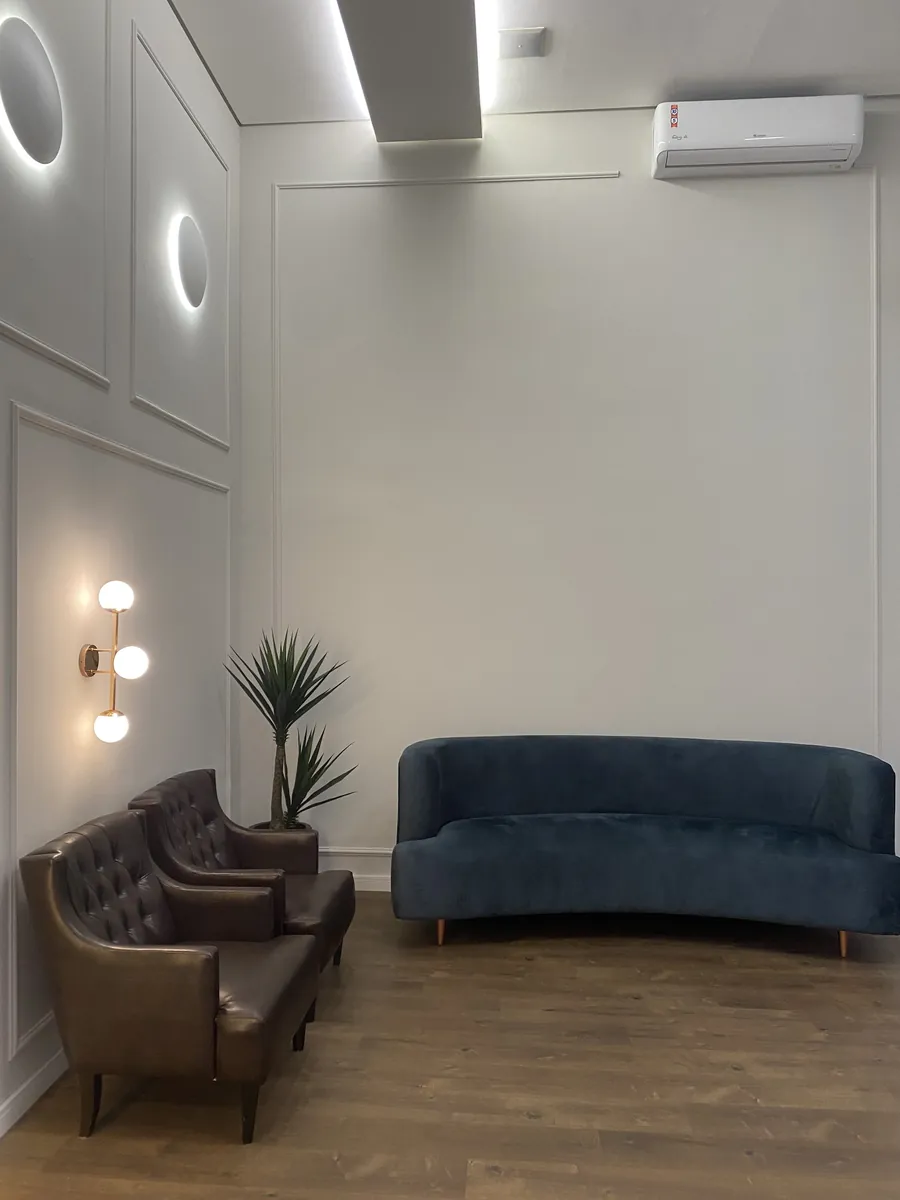 Poltronas de couro e sofá azul-petróleo sob uma luminária em anel